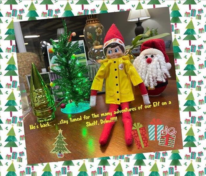Photo shows our Elf on the Shelf in a yellow rain coat with text overlay that states he is back and to stay tuned