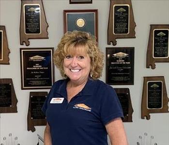 Photo of female employee smiling in front of wall with awards hanging